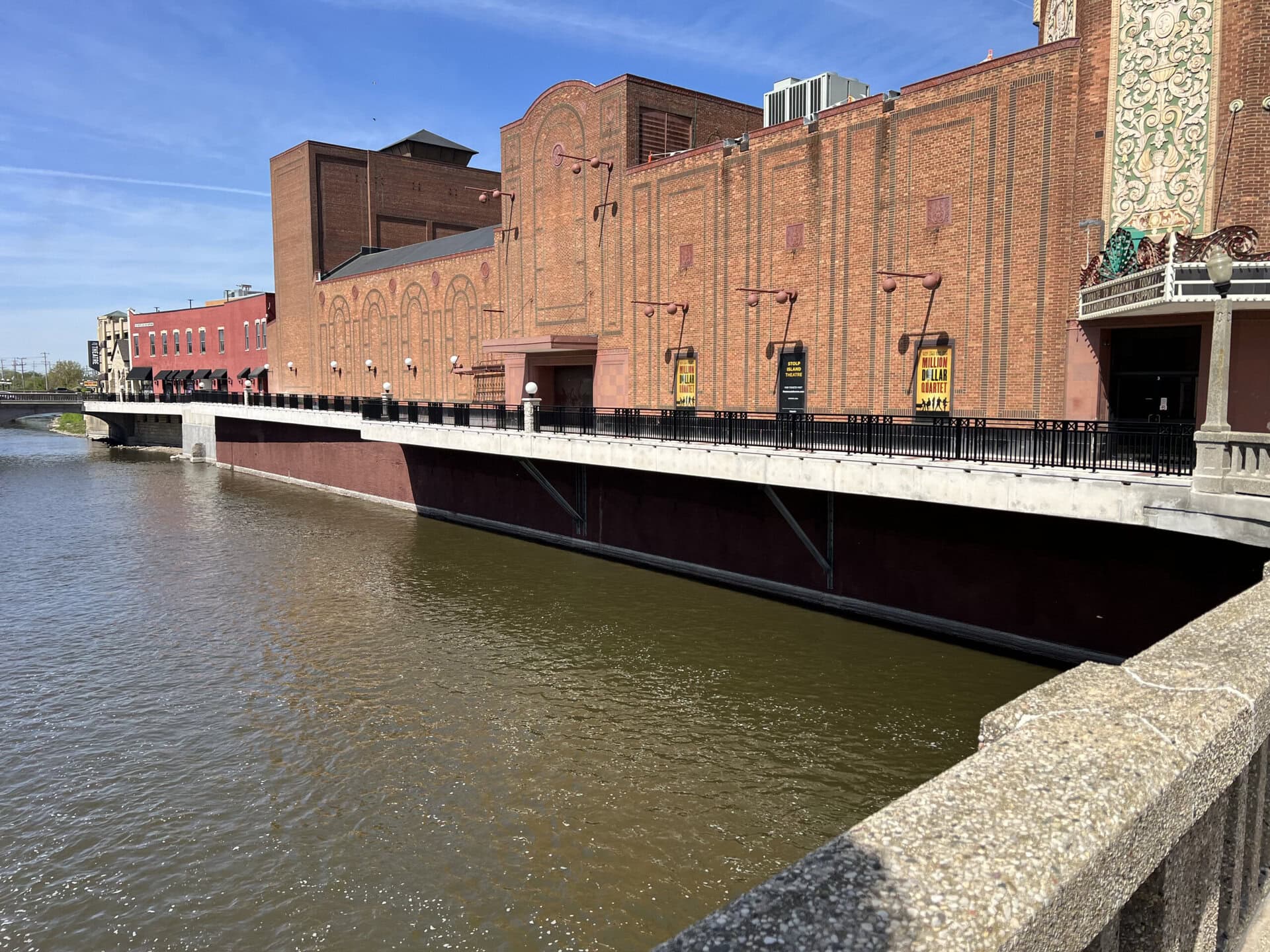 Modern brick building by the water with construction signage, showcasing urban development.